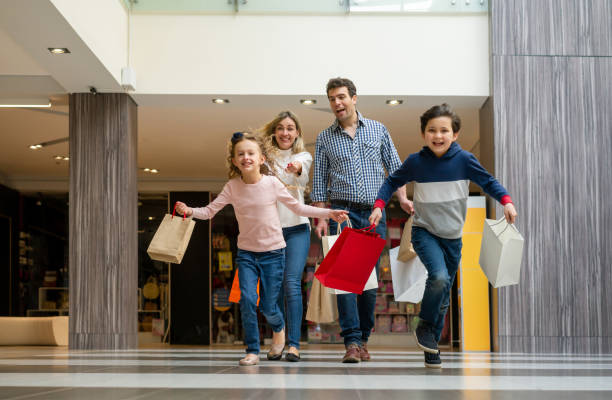 shopping in famiglia eccitato e bambini che corrono al centro commerciale con borse - family fun running couple foto e immagini stock