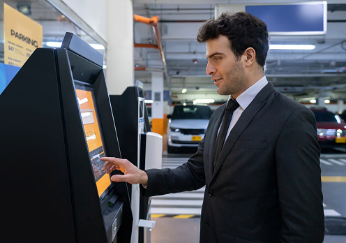 Latin American man at the mall paying the parking lot on a machine. **DESIGN ON SCREEN WAS MADE FROM SCRATCH BY US**