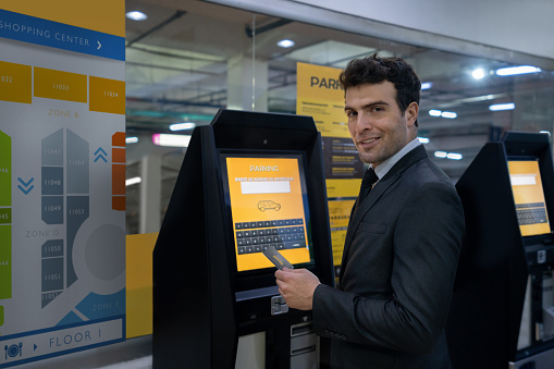 Latin American man at the mall paying the parking lot on a machine and looking at the camera smiling. **DESIGN ON SCREEN AND MAP WERE MADE FROM SCRATCH BY US**