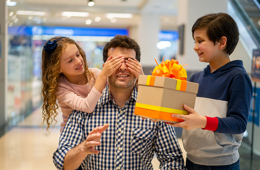 Sweet Kids surprising their father with a gift at the mall and covering his eyes with her hands - Father's Day concepts