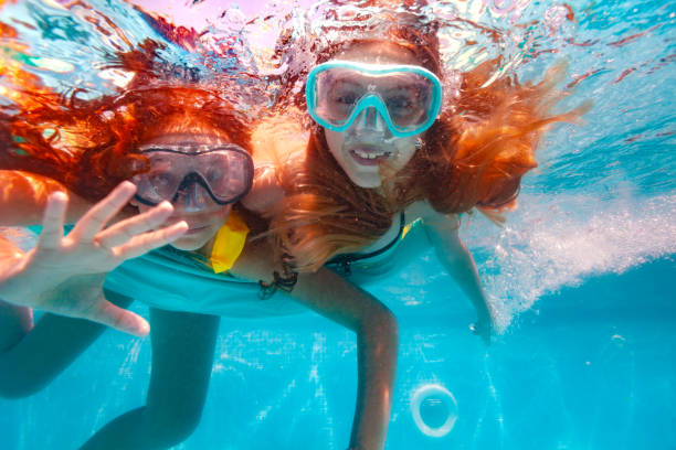 istock Two girls with scuba mask wave hands dive in pool 1330997166