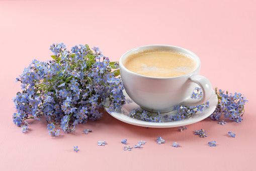 Cup of aromatic coffee and a bouquet of forget-me-nots on a pink background.