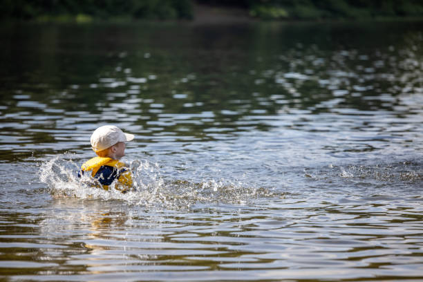 ragazzo che nuota nel lago durante l'estate - life jacket little boys lake jumping foto e immagini stock