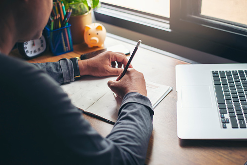 Man Hand of planner writing and plan daily appointment on Calendar book. Senior man mark and noted schedule (holiday trip) on diary at business office desk. Calendar reminder event for planner concept