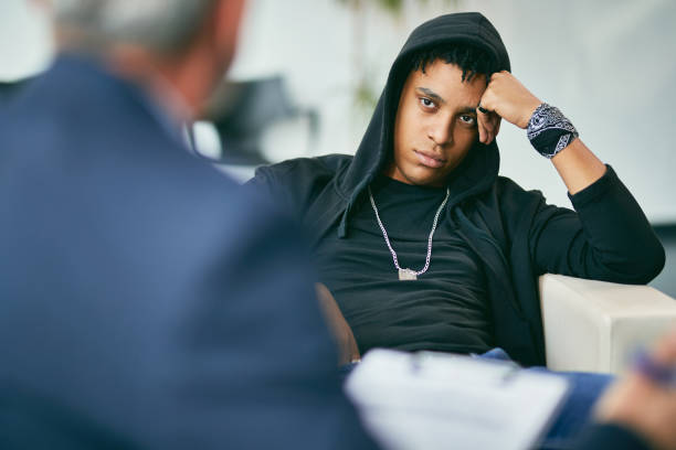 African American teenager having a meeting with psychotherapists at counselling center. Black male adolescent listening to his counsellor during therapy session at psychotherapist's. insurrection stock pictures, royalty-free photos & images