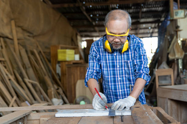 istock Asian senior male carpenter using ruler and pencil at the carpentry workshop. Joiner wearing safety goggles working with tape measure in his workplace 1331030901