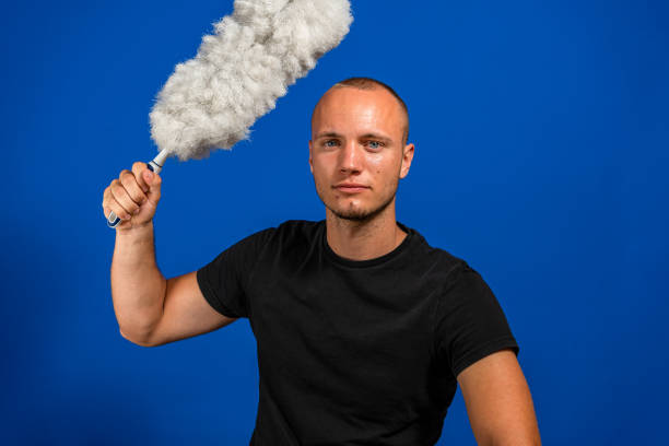 istock Caucasian young man posing funny with a cleaning duster on blue studio background. Cleaning concept 1331032705