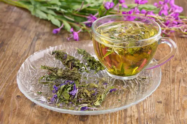 Tea drink from cypress, in a glass cup on the wooden surface of the table. Flowers and leaves of the plant (Chamerion angustifolium)