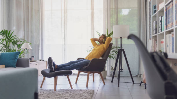 jeune homme portant des écouteurs et écoutant de la musique - armchair comfortable relaxation headphones photos et images de collection