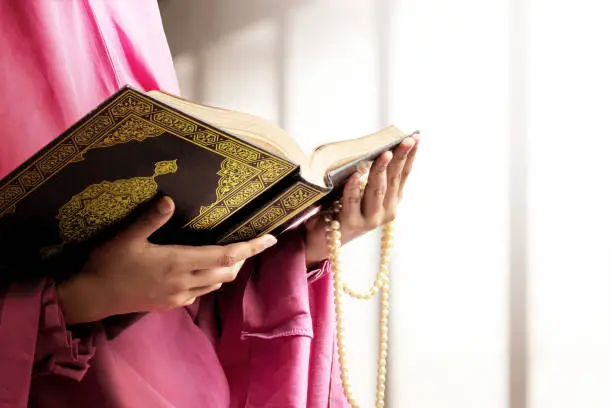 Muslim woman in a veil holding prayer beads and the Quran on the mosque
