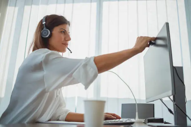 Photo of Businesswoman sitting in her office with headset on and turning on webcam for video conference