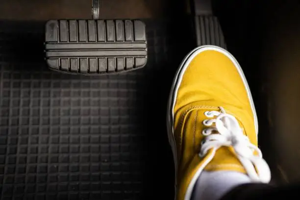 Photo of A man in yellow sneakers is stepping on the accelerator of a car.