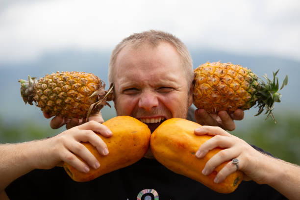two Caucasian hipsters play with papaya and pineapple  outdoors, vegetarian