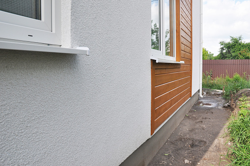 Modern house facade insulation under plastering, stucco and wood wall siding. The combination of stucco and wood siding, wood cladding on the external house wall.