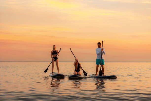 group of caucasian people swimming on a sup boards at the ocean. sport activity of friends at the vacation. summer sport and recreation. copy space - paddle surfing stockfoto's en -beelden