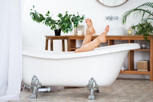 Woman relaxing in bathroom, slim legs with smooth skin, foot care concept, home interior