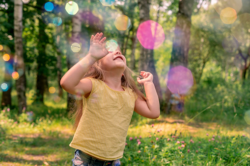 happy caucasian child girl in a yellow t-shirt catches a lot of soap bubbles on a summer day. outdoor activity, rainbow