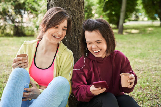 Girls laughing out loud and turning on songs on her smartphone Waist up portrait view of female little person laughing out loud and turning on songs on her smartphone while listening to music with her best friend in nature dwarf stock pictures, royalty-free photos & images
