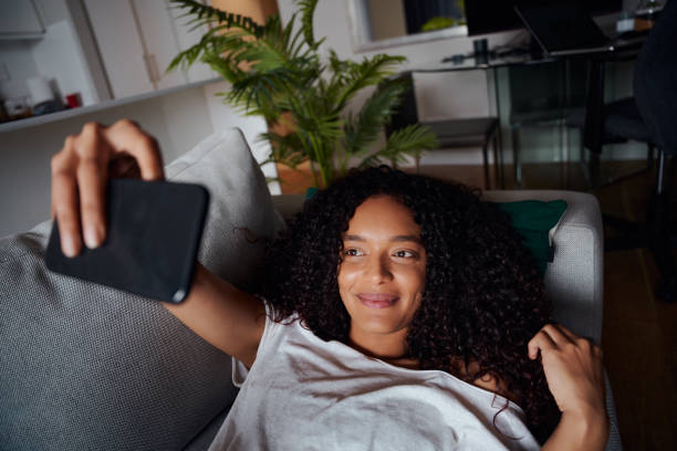 istock Mixed race female taking selfies while lying on couch smiling 1331058039