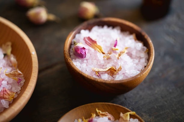 Sea salt scented with rose aroma, in wooden bowls, mixed with dried rose petals and rose buds,von wooden background