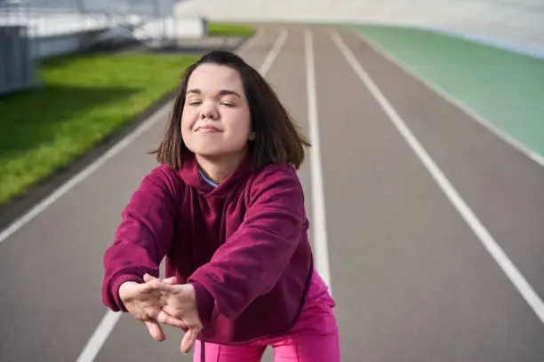 Cropped view of a caucasian ,calm, female, little person warming up at the stadium and stretching her hands before the training. Exercises at the fresh air 