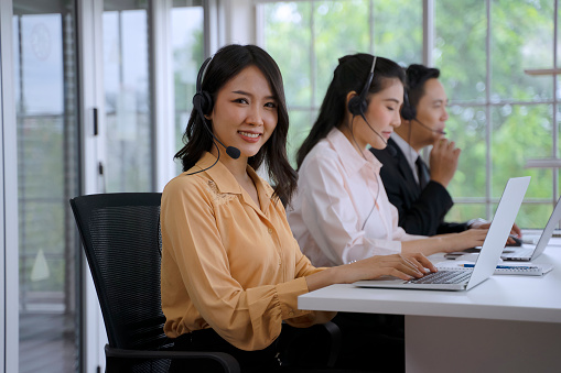 Operator are working  at call center. They are using computer and wearing headphone. Happiness mood and teamwork.