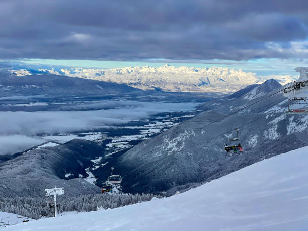 Scenic view of an operating skilift moving up a slope overlooking wintry valley. Scenic view of an operating skilift in the Slovenian mountains moving up a groomed slope overlooking wintry valley. Breathtaking view of a distant mountain range from the summit of a ski resort slope. krvavec stock pictures, royalty-free photos & images