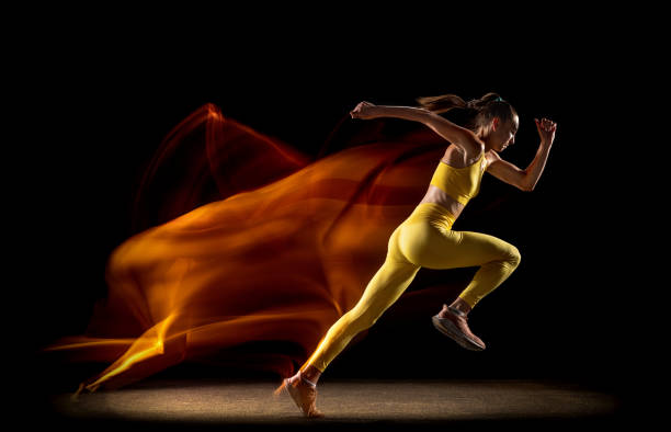 Running. Young woman, female professional track athlete training isolated over black studio background in mixed neon lights. Concept of sport, healthy lifestyle, motion. Copy space for ad.