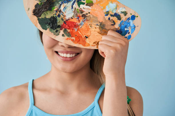 istock Woman hiding her face behind palette with paints while shooting at the studio 1331064644