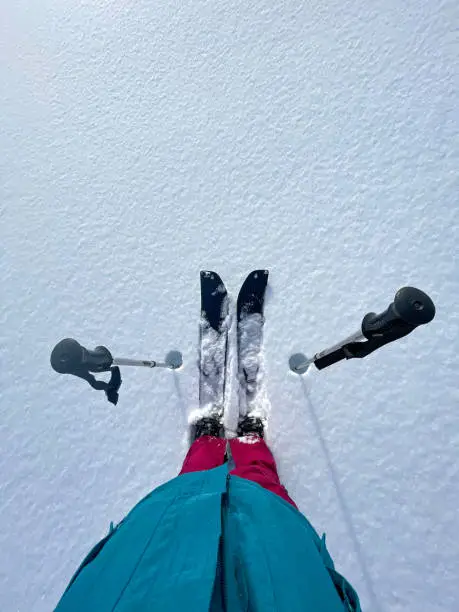 POV: Looking down at your splitboard and poles while enjoying an active winter vacation in the picturesque snowy Alps. First person shot of your ski touring equipment as you stand in deep powder snow.