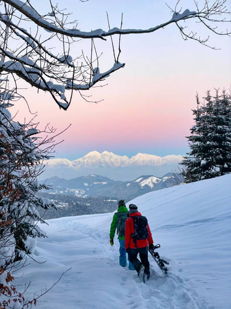 istock VERTICAL: Two unrecognizable snowboarders hike along the snowy meadow at sunset. 1331065593