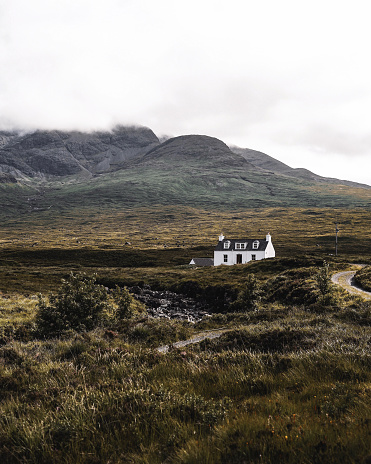 A portrait image of a beautiful lone White House at the base of some mountains in Sligachan, Isle of Skye, Scotland.