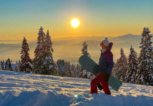 CLOSE UP: Young female snowboarder hikes up ungroomed snowy slope at sunset. CLOSE UP, LENS FLARE: Young female snowboarder hikes up ungroomed snowy slope at sunset. Golden winter morning sun rises above the idyllic snowy mountain and woman on snowboarding trip hiking up hill. krvavec stock pictures, royalty-free photos & images