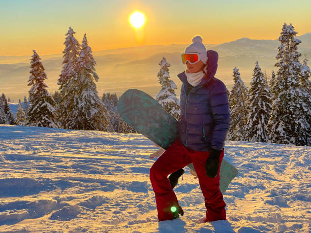 CLOSE UP: Golden winter morning sun rises above mountain and hiking snowboarder. CLOSE UP, LENS FLARE: Golden winter morning sun rises above the idyllic snowy mountain and woman on snowboarding trip hiking up hill. Young female snowboarder hikes up ungroomed snowy slope at sunset. krvavec stock pictures, royalty-free photos & images