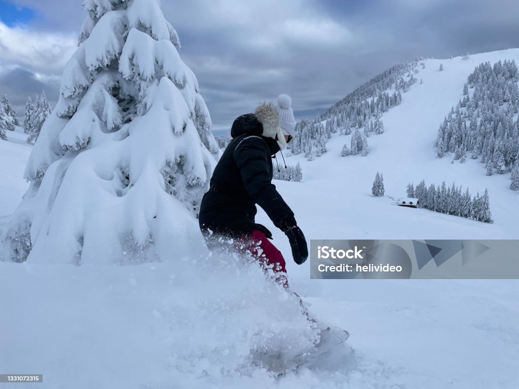 CLOSE UP: Young woman shreds fresh powder while snowboarding in backcountry. CLOSE UP: Young woman shreds fresh powder snow while snowboarding in backcountry. Unrecognizable female snowboarder on active winter vacation in Krvavec rides in the picturesque snowy wilderness. 25-29 Years Stock Photo