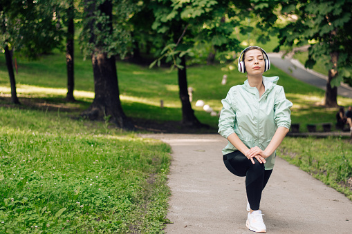 Young woman with headphones warming up for exercising in the park.