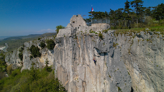 AERIAL: Drone point of view of a female rock climber training in sunny Osp. Breathtaking flying view of the scenic landscape surrounding an athletic young woman rock climbing in idyllic rural Slovenia