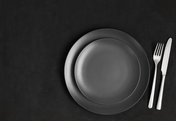 istock Black table setting. Empty black plate and silver cutlery on a dark concrete background. View from above. Copy space. 1331075201