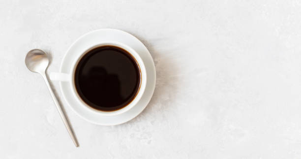 istock Cup of black coffee on a white concrete background. Coffee cup and silver spoon. Copy space, top view. 1331075349