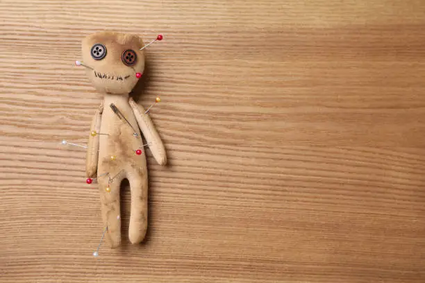 Voodoo doll pierced with pins on wooden table, top view. Space for text