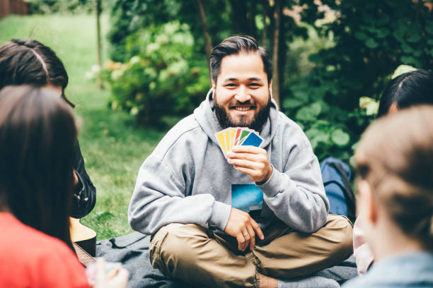 Happy friends having picnic in the park. Friend having fun, smiling and playing board games outside. Happy friends having picnic in the park. Friend having fun, smiling and playing board games outside. friends playing cards stock pictures, royalty-free photos & images