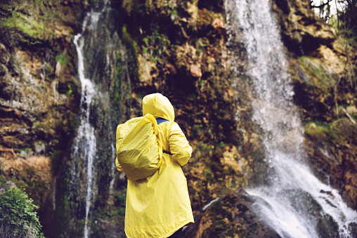 Young man in yellow raincoat exploring the beautiful sunny waterfall in the mountains
