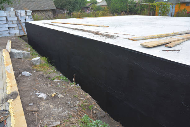 istock Basement and foundation construction and waterproofing by applying asphalt, bitumen or rubber based tar and digging a drainage trench. Exterior foundation walls sprayed with tar. 1331080118