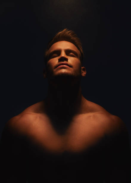 shot of a handsome young man with no shirt on standing in the shadows - sensuality men shirtless studio shot imagens e fotografias de stock