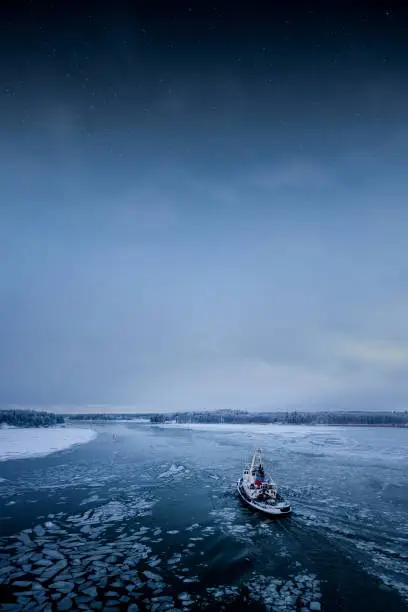 Photo of Tug boat in calm icy water in winter and stars in the sky. Peaceful artistic image.