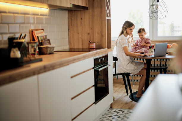 istock Stay at mother home sitting in kitchen and getting work done while her baby girl helping her. 1331084676
