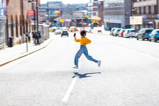 Curly young woman running across the street - Young black woman wearing yellow top crossing the street on a rush - lifestyle and commuting concepts