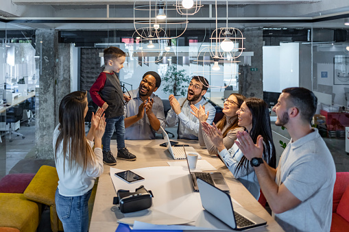 Multi ethnic group of coworkers in office have meeting. They have presentation, mother standing next to her son and explaining new strategy.