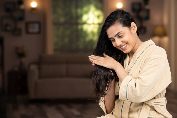 scatto di una giovane donna in accappatoio facendo massaggio ai capelli a casa - cura dei capelli foto e immagini stock