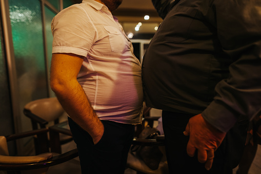 Two fat men standing belly to belly indoors
